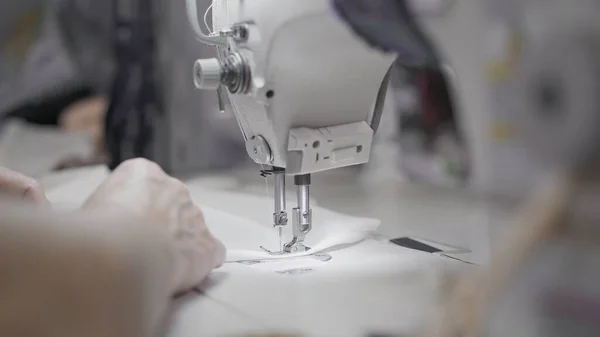 Sewing white cloth on a white sewing machine close up, female hands