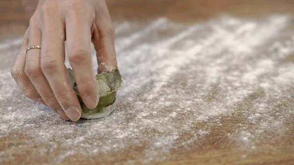 Hand och en grön rå tortellini i mjöl på träbord — Stockfoto