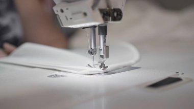 Beyaz bir dikiş makinesine beyaz bez dikiyorum. Yakın plan, bulanık arkaplan.