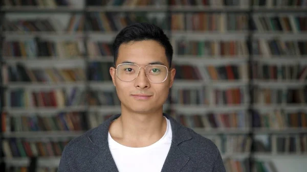 Studente asiatico in giacca grigia su sfondo di librerie sfocate in biblioteca — Foto Stock