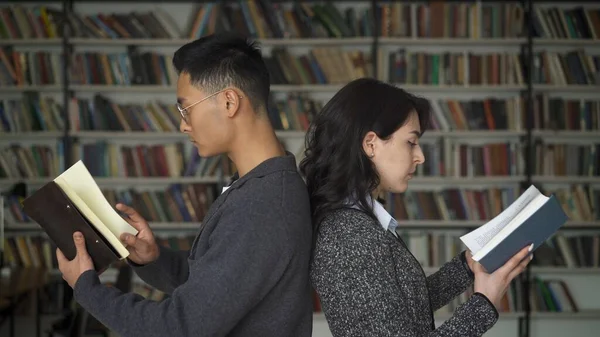 Giovane uomo e donna back to back sullo sfondo di librerie sfocate in biblioteca — Foto Stock