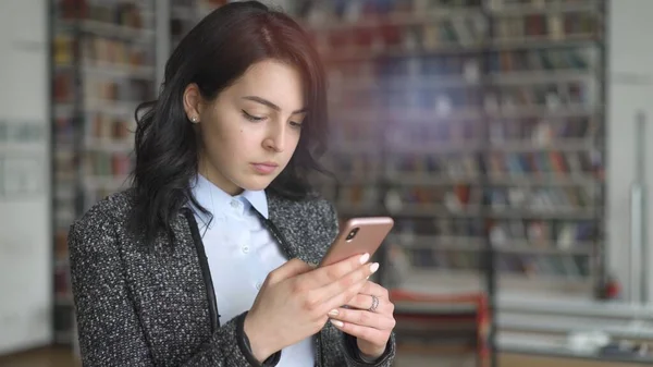 Jonge aziatische vrouw met telefoon in de hand op de achtergrond van boekenplanken, lens flare — Stockfoto