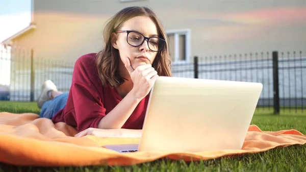 Meisje in bril op zoek laptop aan het werk op het gazon, lens flare — Stockfoto