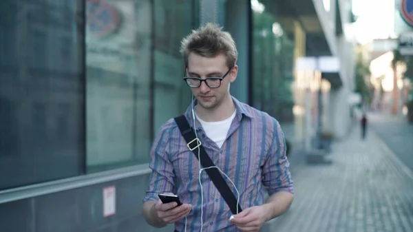 Молодий чоловік з телефоном і навушниками, що йдуть по дорозі, середній постріл — стокове фото