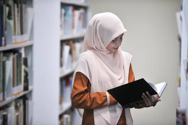 Young hijab student reading a book in a public library.