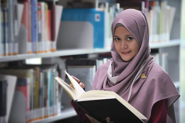Young hijab student reading a book in a public library.