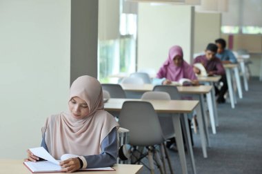Young beautiful hijabi students study in a library. (Selective focus) clipart