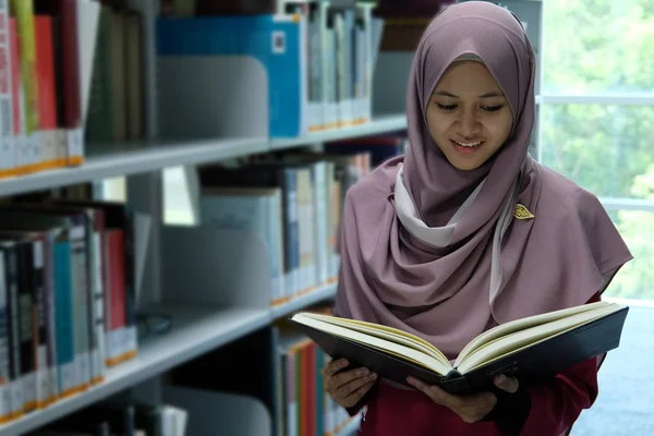 A beautiful young hijab woman reading a book after picking a book from bookshelf in a library.