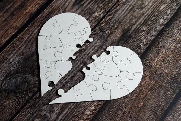 Love shape separated from a shape love white puzzle on top of wooden table. Heart broken and disappointment conceptual.