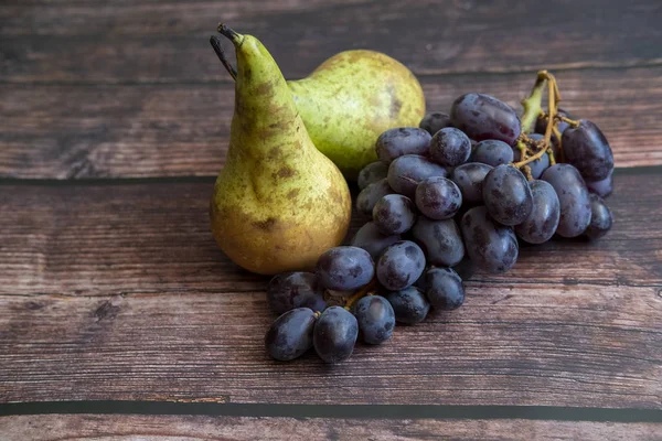 Konferenzbirne auch als Pyrus communis bekannt und kernlose rote Traube auf dem Holztisch. — Stockfoto