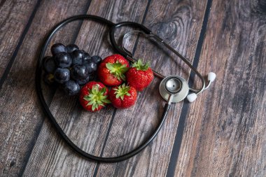 Kırmızı İskoç çilekleri ve ahşap masanın üstünde steteskoplu siyah üzümler. Tıbbi ve sağlıklı gıda kavramsal.