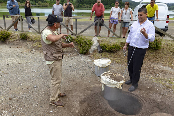 FURNAS, PORTUGAL - AUGUST 4: An unidentified chef and his helper dig out Cozido, an Azores meal cooked in the ground near thermal vents at Fumarolas da Lagoa das Furnas in Furnas, Portugal on August 4, 2017.