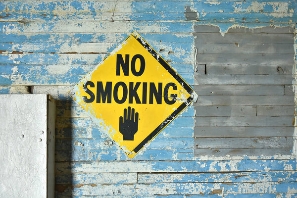 An image of an old vintage no smoking sign posted to an old weathered blue wall. 