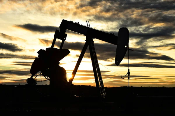 A silhouette image of a working oil and gas industry pump jack at sunset.