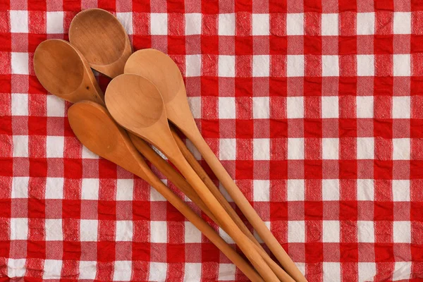 A top view image of several wooden mixing spoons on a red and white checkered table cloth.
