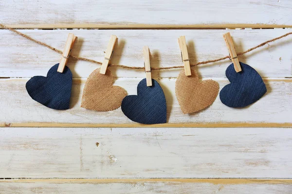 A close up image of several heart shaped symbols hung by clothes pins on a wooden background.
