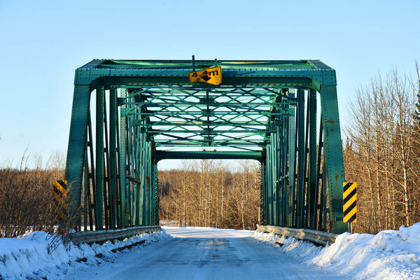 An image of an old green single lane bridge on a rural country road in winter. 