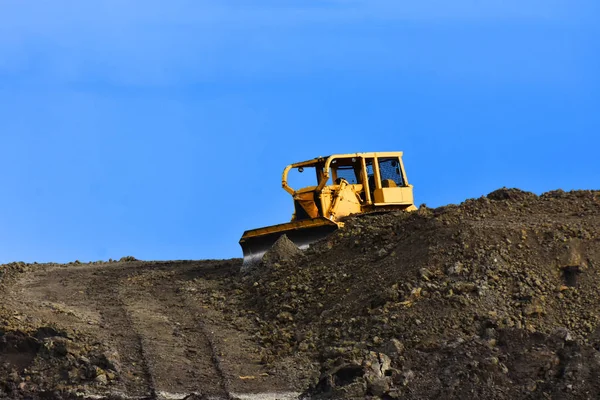 An image of a large yellow earth mover on top of a pile of dirt at a construction site.