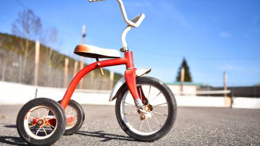 Boş bir okul oyun alanında eski bir kırmızı üç tekerlekli bisiklet görüntüsü. 