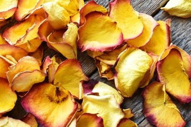 Eski ahşap bir masa üzerinde sarı ve kırmızı kurutulmuş gül yaprakları yakın bir görüntü. 