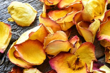 Eski ahşap bir masa üzerinde sarı ve kırmızı kurutulmuş gül yaprakları yakın bir görüntü. 