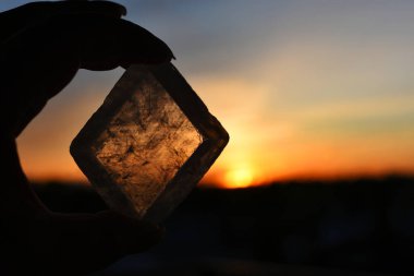 A close up image of transparent champagne calcite held against a glowing orange sunset.  clipart