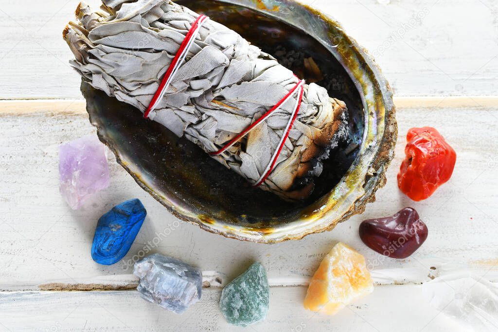 A close up image of Chakra healing crystals with white sage smudge sticks and orange sacred feather. 