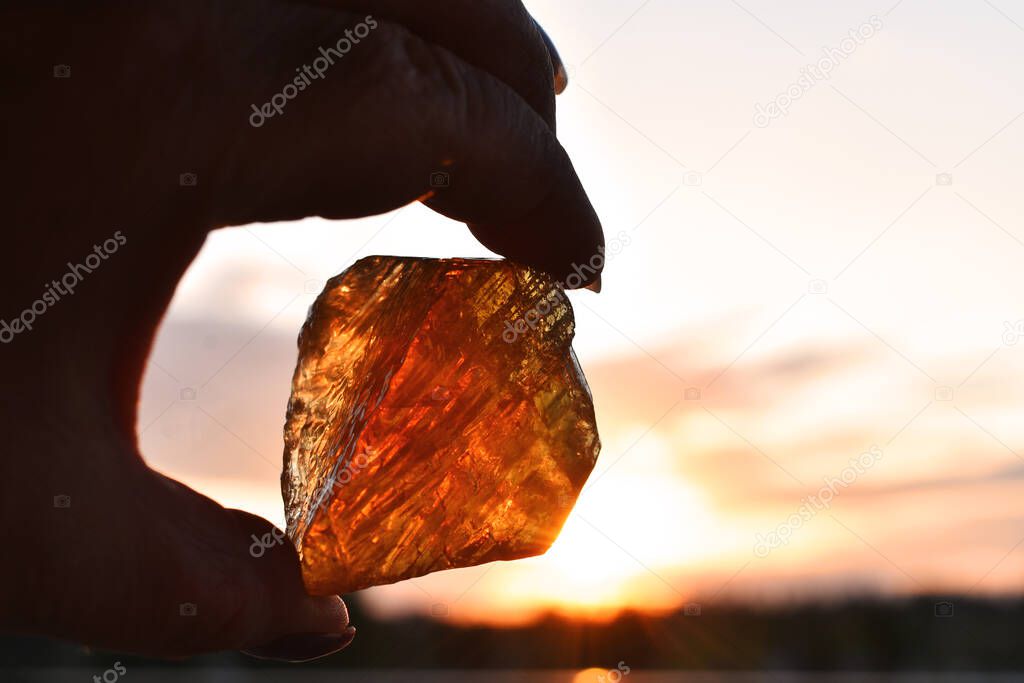 An silhouette image of a hand holding a piece of hone calcite against a glowing sunset. 