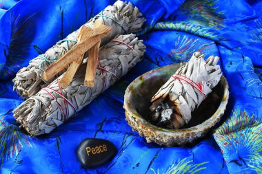 And image of white sage bundles in an abalone shell on a bright blue silk background.  clipart