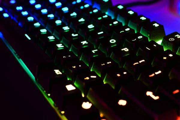 A low angle image of a back lit computer keyboard with red, blue, and green lights. .