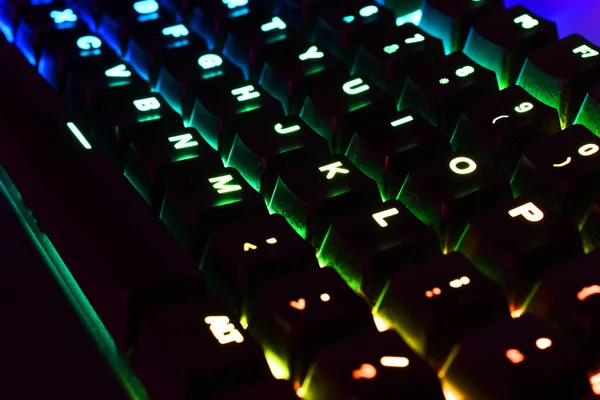 A low angle image of a back lit computer keyboard with red, blue, and green lights. .