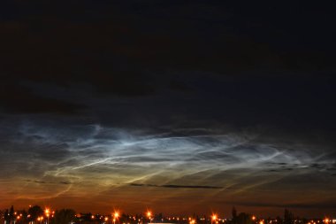 An image of noctilucent clouds over an small urban city during the early morning hours.  clipart