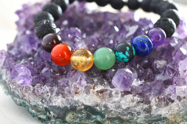 A close up image of a beautiful chakra bracelet charging on a purple amethyst geode.