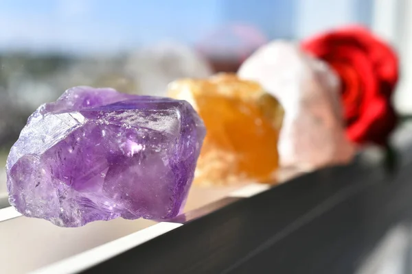 A close up image of three healing crystals charging in the sunlight on a window ledge.