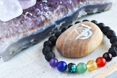 Ahşap bir masanın üstünde el yapımı çakra bileziği ve ametist jeotun yakın plan görüntüsü.. 