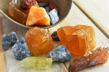 A close up image of a hand made pottery bowl and red, yellow, blue, and green calcite crystals.  clipart