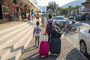 Türkiye, İçmeler, Ağustos 2017: Bir kız ve bir çocuk bir çanta ile sokakta yürüyor. Otelin kontrol edin. Otel arama.