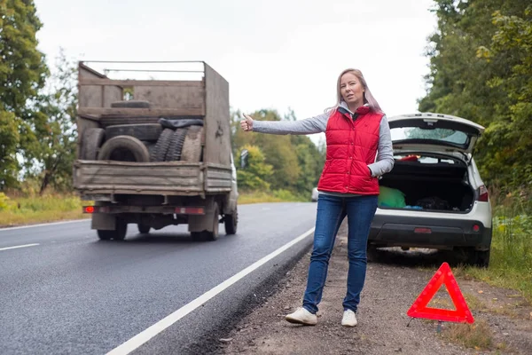 Sinir bozucu kadın sürücü yakınındaki kırık bir araba. Bir ülke yolda bir araba, bir kadın bir yolculuk yakalar.