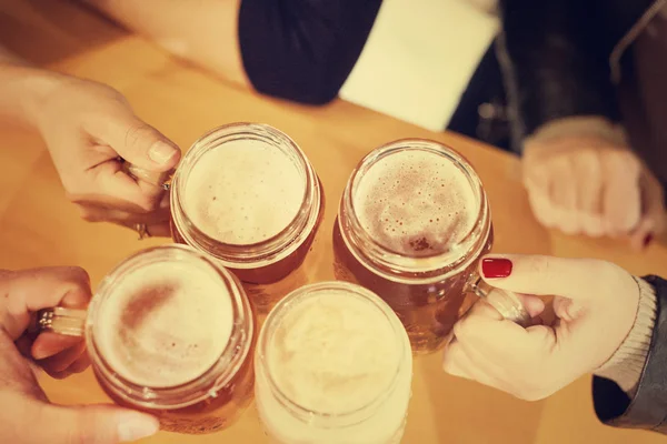 Top view of friends cheering with home brew in pub bar restaurant - Young people hands toasting and beers half pint - Friendship and party concept - Warm matte filter - Focus on bottom hand