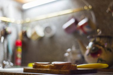 Ahşap masada kesme tahtasında sosis, mutfak bıçağı, ekmek parçaları. 