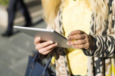 Şehir caddede yürüyüş tablet bilgisayar kullanan genç sarışın iş kadın. Şık moda modeli güneş gözlüğü