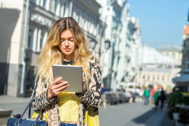 Şehir caddede yürüyüş tablet bilgisayar kullanan genç sarışın iş kadın. Şık moda modeli güneş gözlüğü