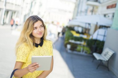 Şehir caddede yürüyüş tablet bilgisayar kullanan genç sarışın iş kadın. Şık moda modeli güneş gözlüğü