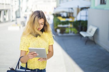 Şehir caddede yürüyüş tablet bilgisayar kullanan genç sarışın iş kadın. Şık moda modeli güneş gözlüğü