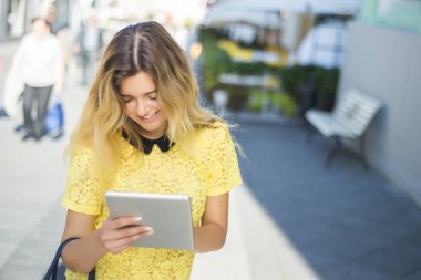 Şehir caddede yürüyüş tablet bilgisayar kullanan genç sarışın iş kadın. Şık moda modeli güneş gözlüğü