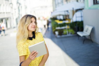 Şehir caddede yürüyüş tablet bilgisayar kullanan genç sarışın iş kadın. Şık moda modeli güneş gözlüğü