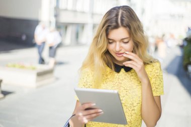 Şehir caddede yürüyüş tablet bilgisayar kullanan genç sarışın iş kadın. Şık moda modeli güneş gözlüğü