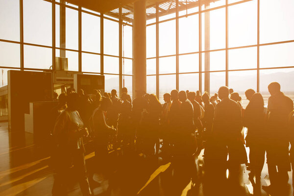 Силуэт толпы людей, ожидающих самолет в терминале аэропорта с горным фоном
