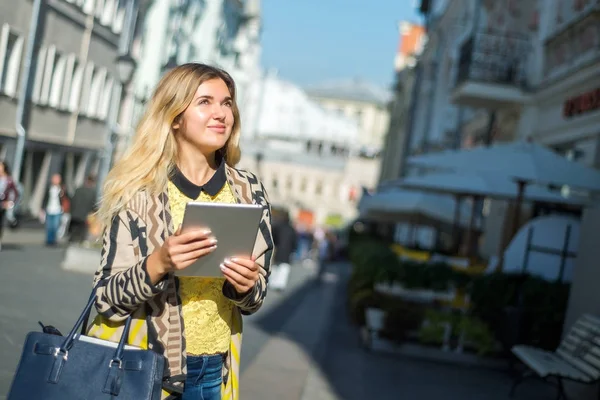 Şehir caddede yürüyüş tablet bilgisayar kullanan genç sarışın iş kadın. Şık moda modeli güneş gözlüğü