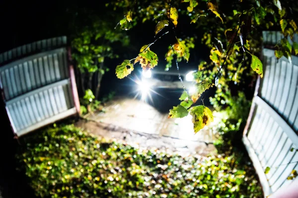 Arabayı geceleri evi toprakları üzerinde duruyor. Çitin üzerinden ışık farlar